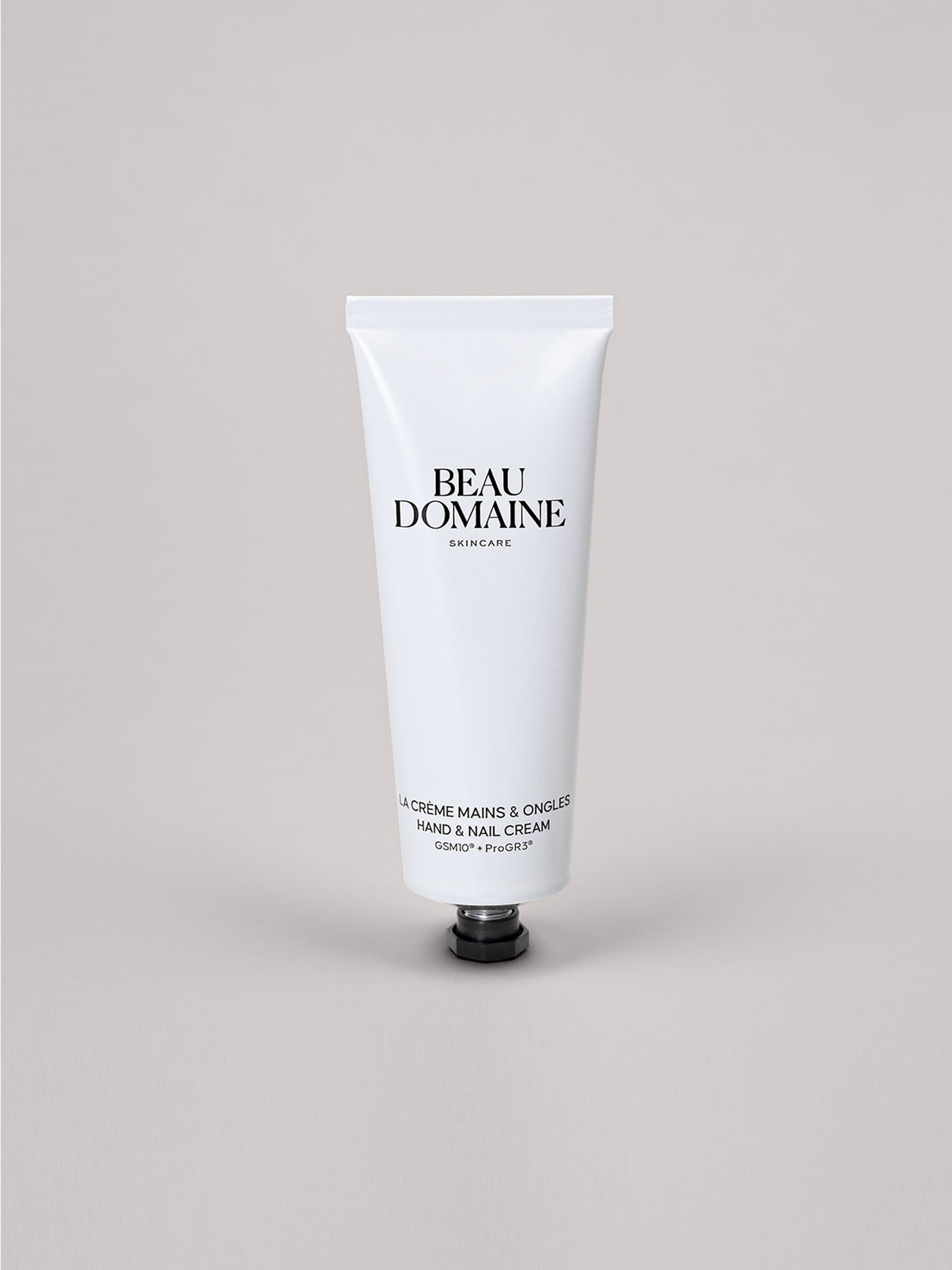 Bisnaga branca do creme para mãos e unhas Beau Domaine sobre fundo cinzento claro.